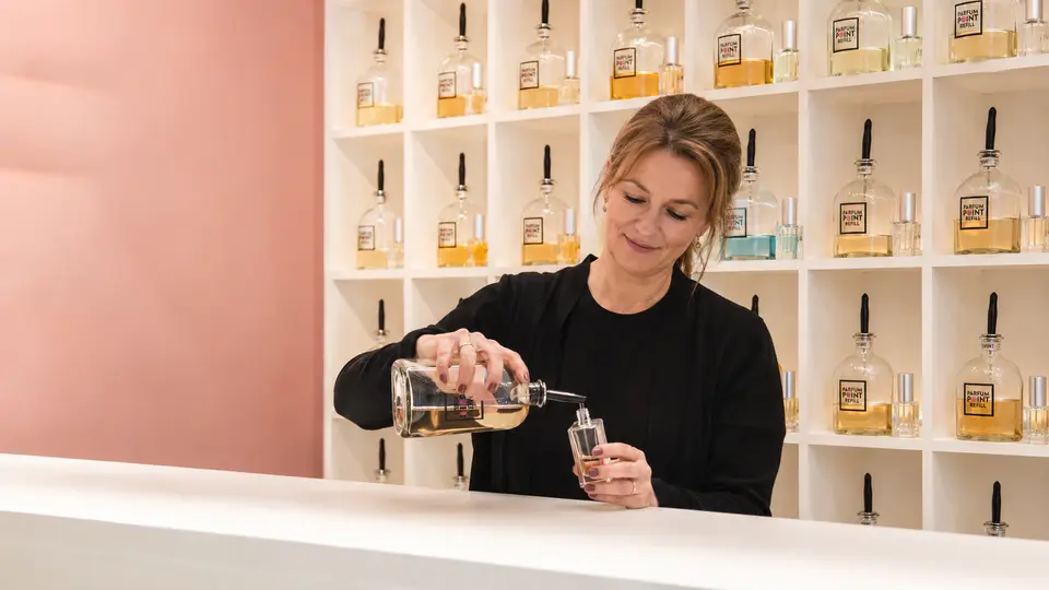 Winkelier vult een parfumflesje uit een schenkfles voor een wand met parfums van ParfumPoint Refill